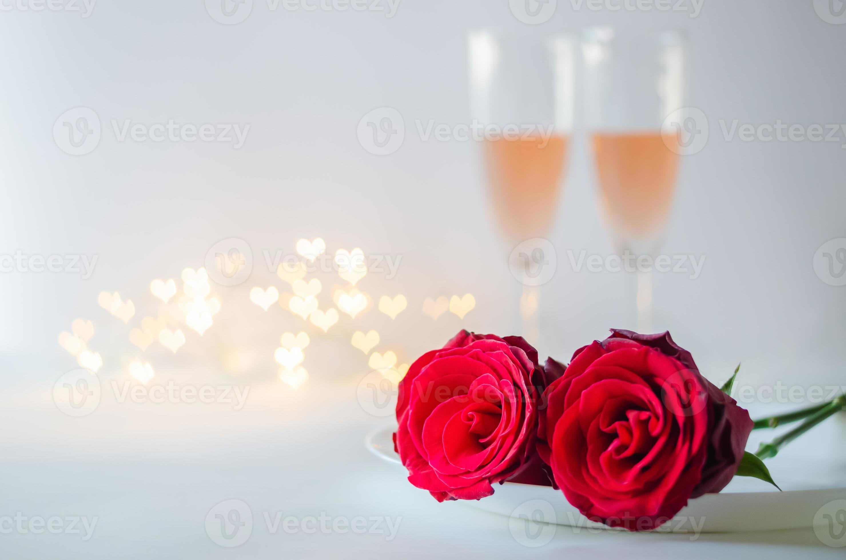 Red roses on plate with glasses of sparkling Rose wine on white background with love shape bokeh