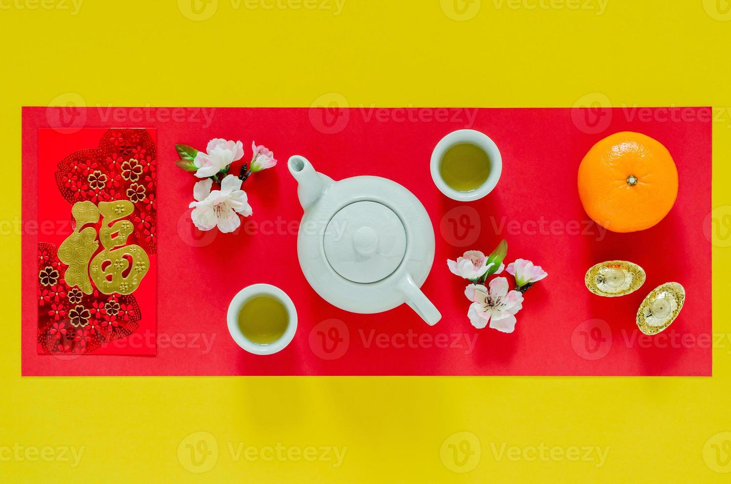 Chinese new year yellow and red background with tea set, chinese blossom flowers, gold ingots, oranges and red envelope packet or ang bao word means wealth. photo