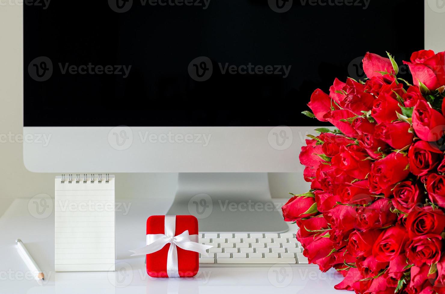 Red gift box and red roses bouquet on working desk with small paper note to surprise on anniversary or Valentine day concept. photo