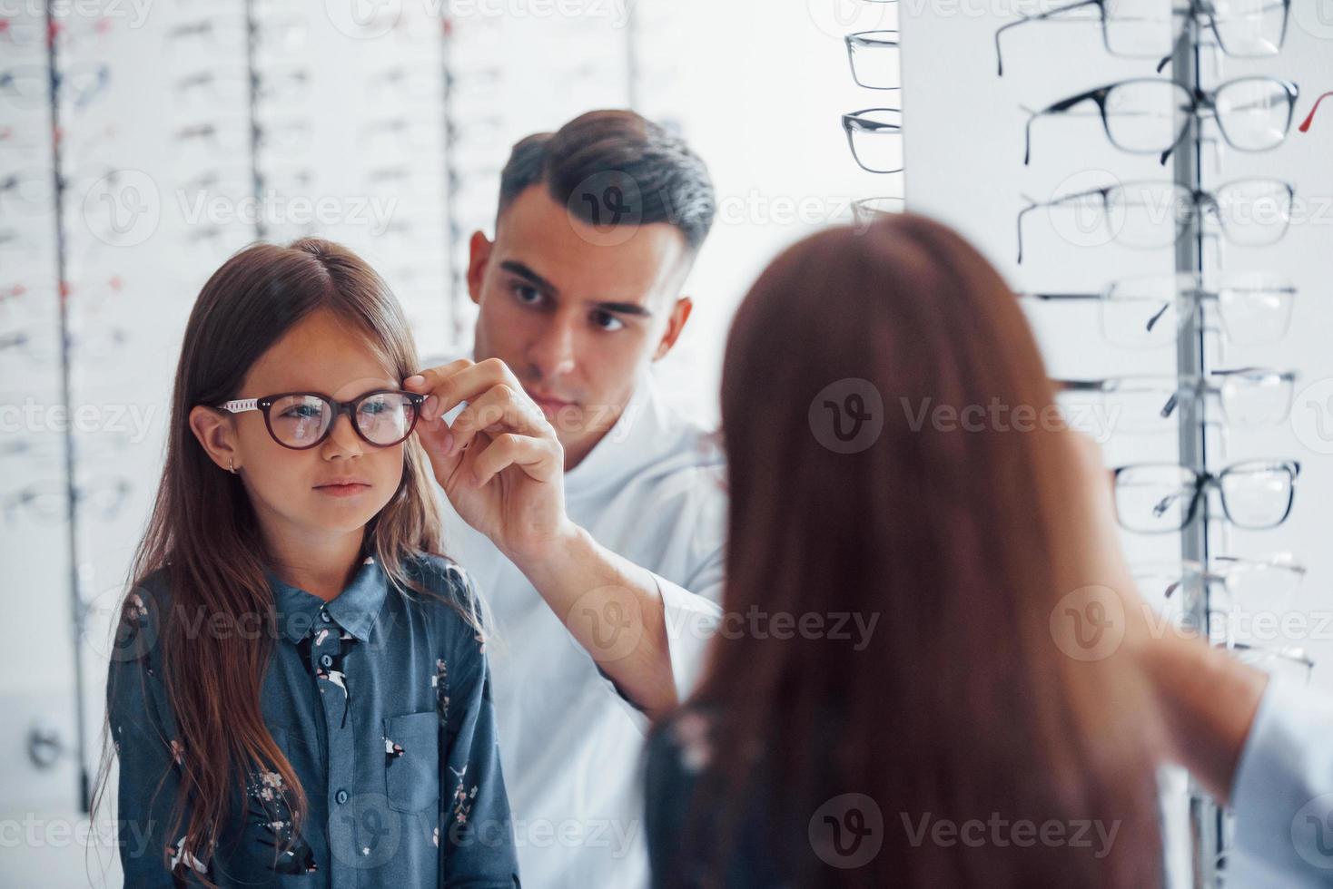 el joven pediatra de bata blanca ayuda a conseguir gafas nuevas para la niña foto