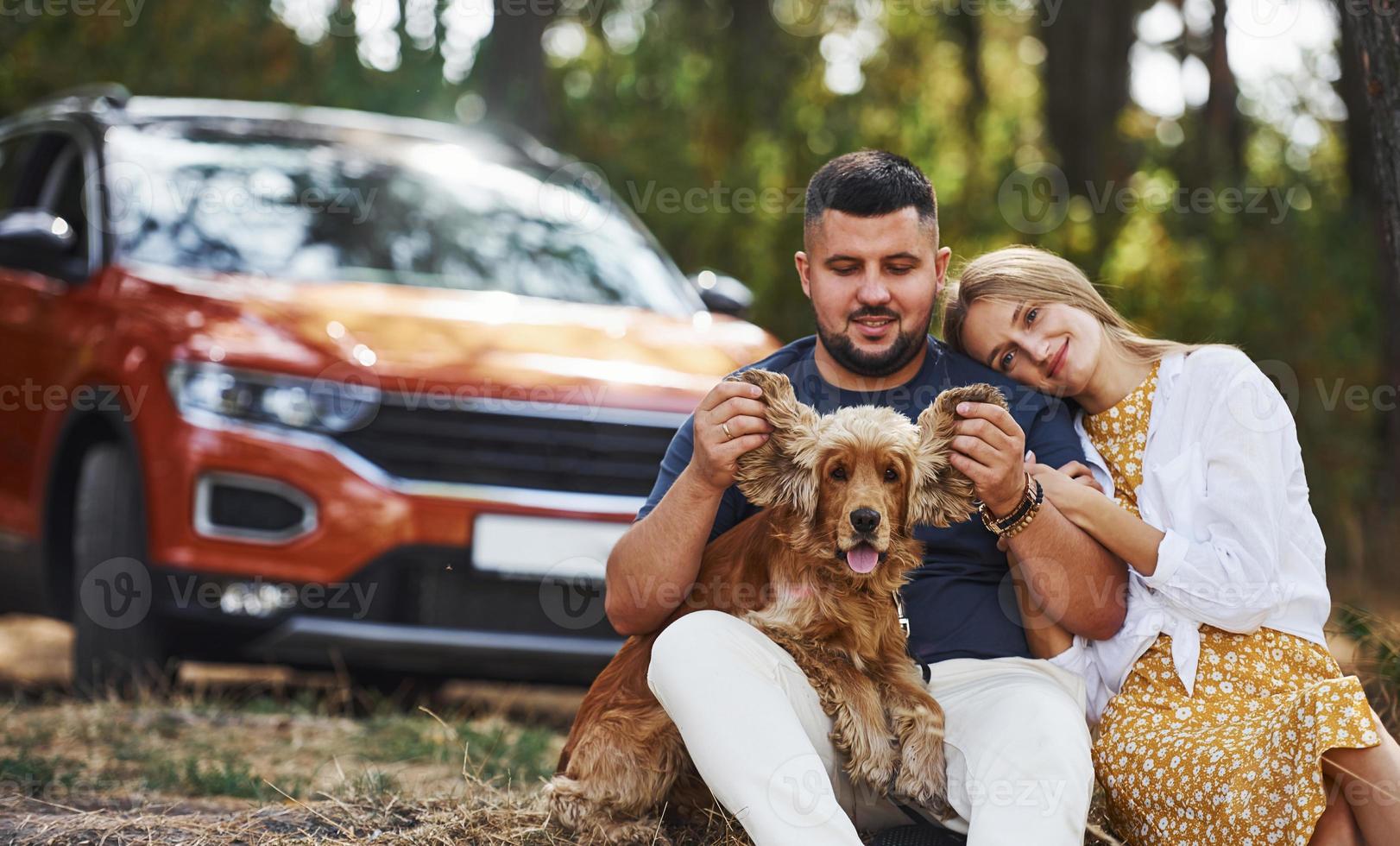 Couple with dog have weekend outdoors in the forest with car behind them photo