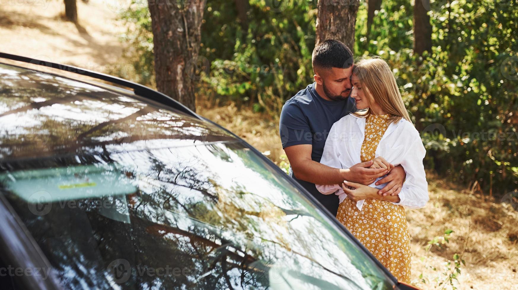 Couple embracing each other in the forest near modern car photo