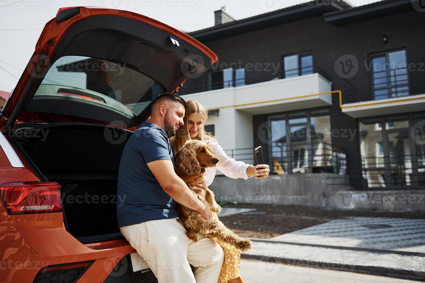 Trunk is open. Lovely couple have a walk together with dog outdoors near the car photo