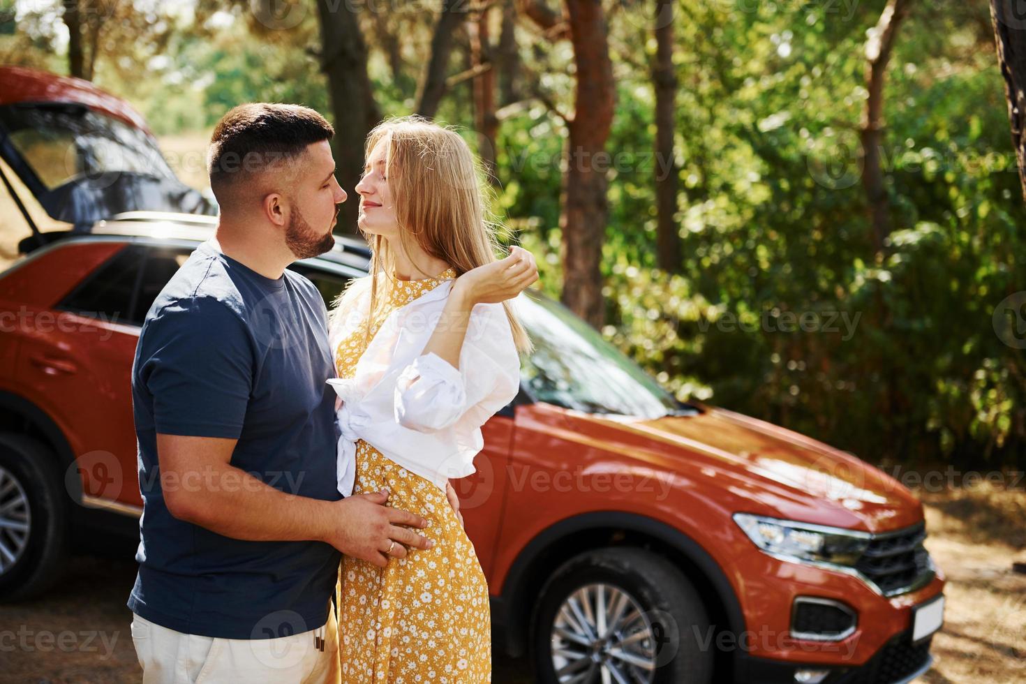 Couple embracing each other in the forest in front of modern car photo