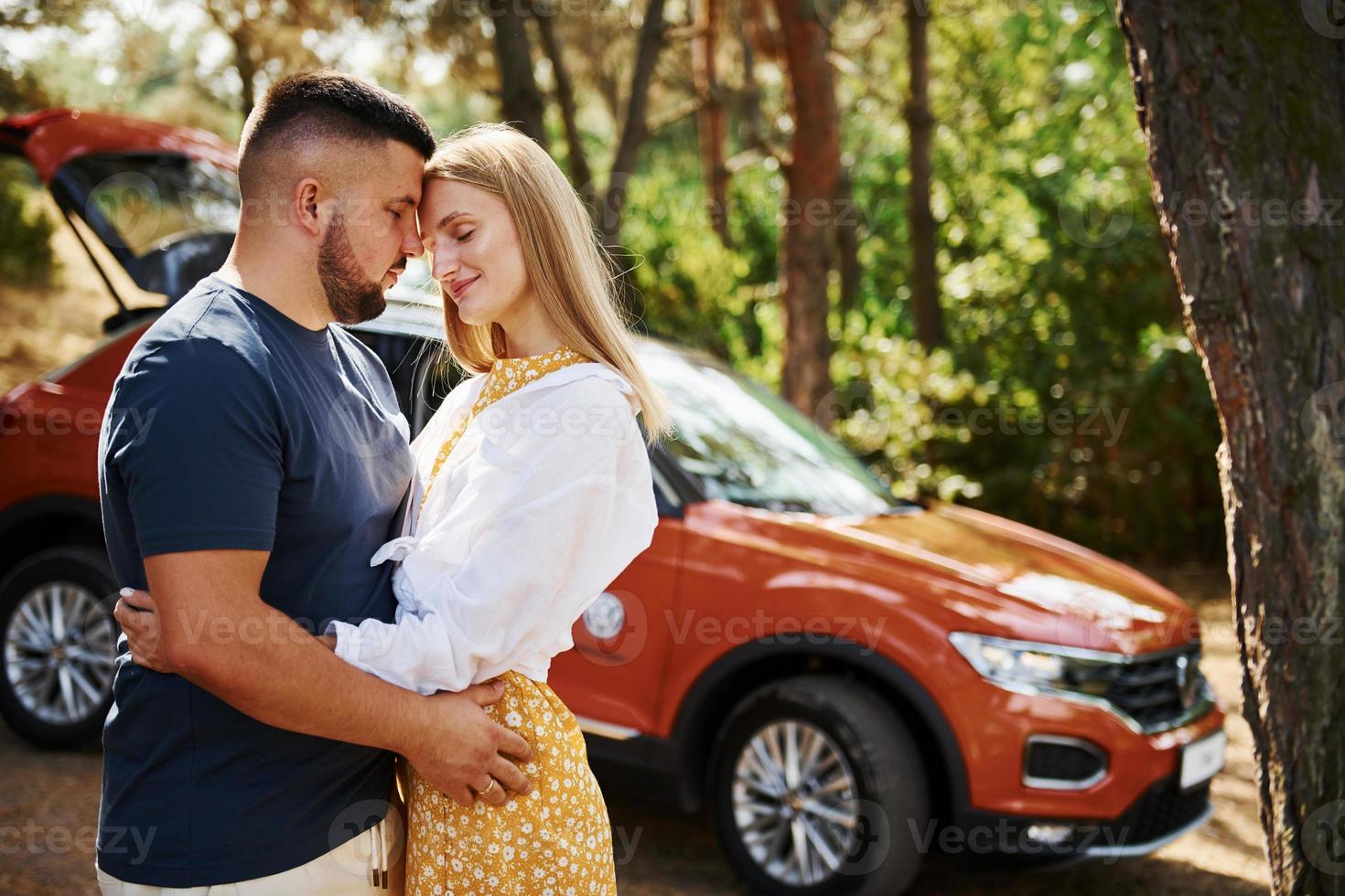Couple embracing each other in the forest in front of modern car photo