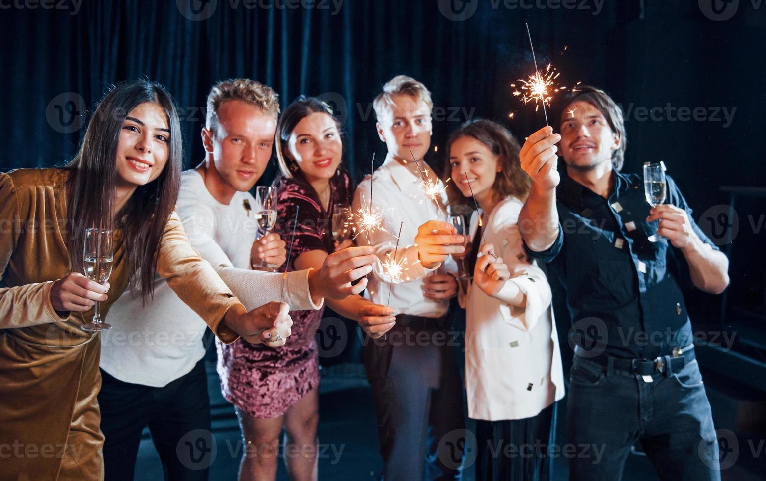 Group of cheerful friends celebrating new year indoors with drinks in hands photo