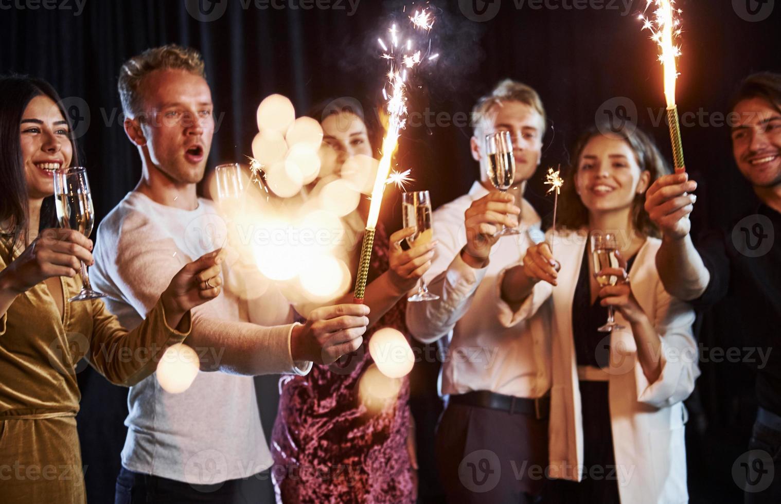 divirtiéndose con bengalas. grupo de amigos alegres celebrando el año nuevo en el interior con bebidas en las manos foto