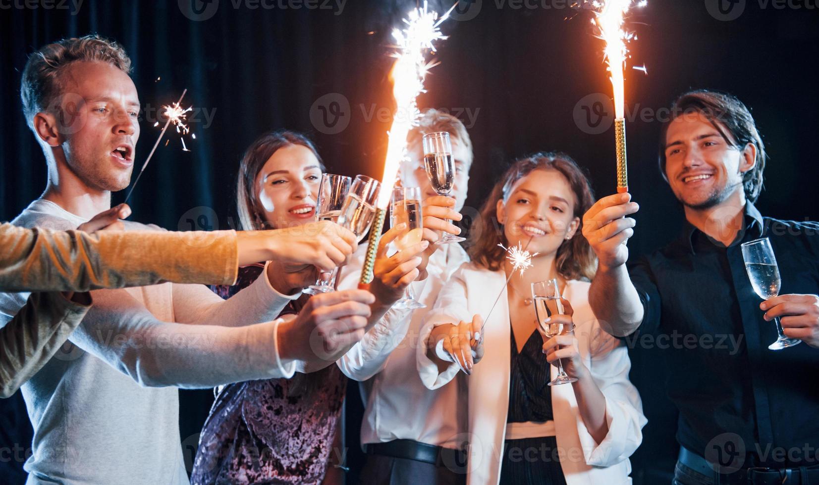 divirtiéndose con bengalas. grupo de amigos alegres celebrando el año nuevo en el interior con bebidas en las manos foto