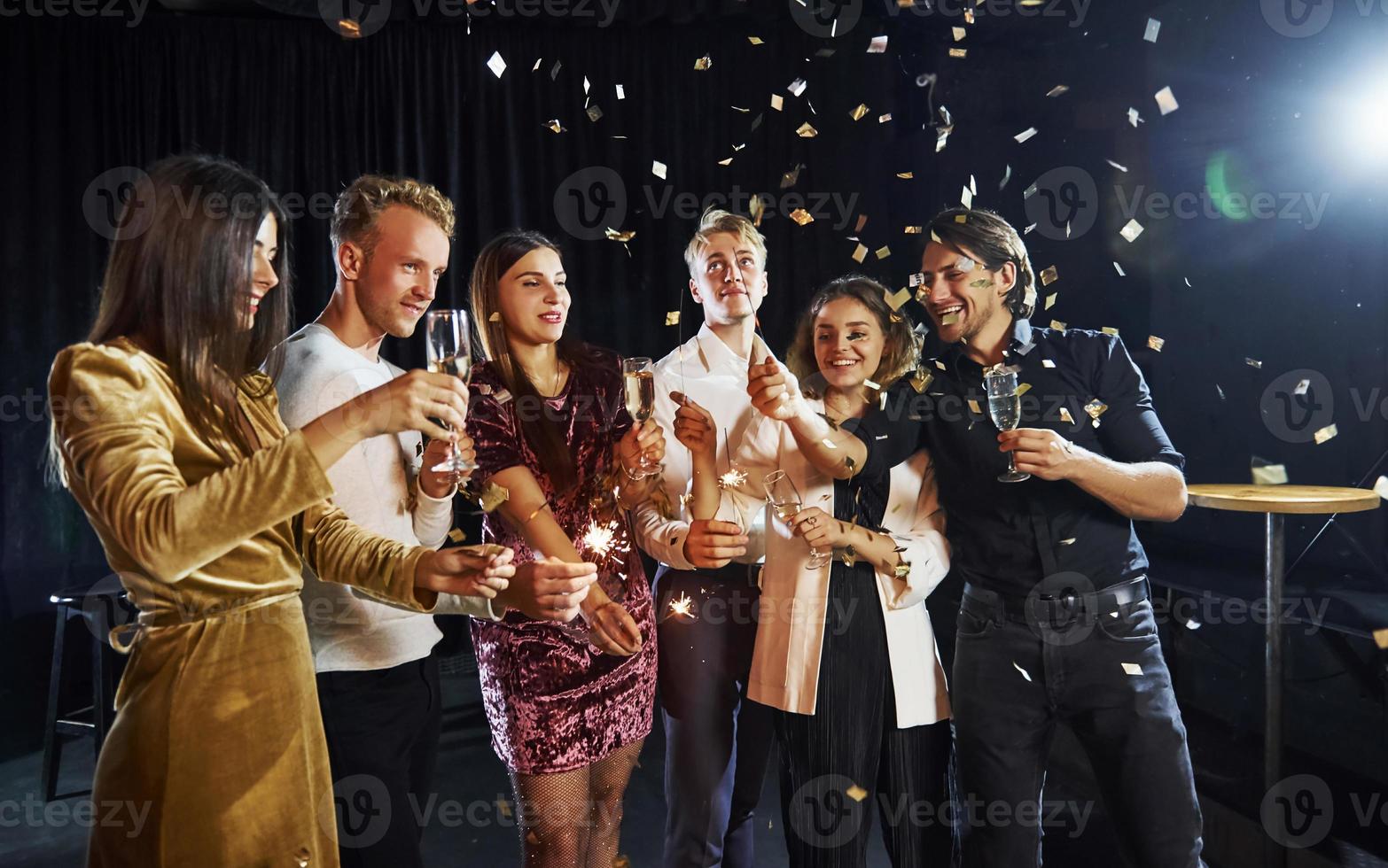 Group of cheerful friends celebrating new year indoors with drinks in hands photo