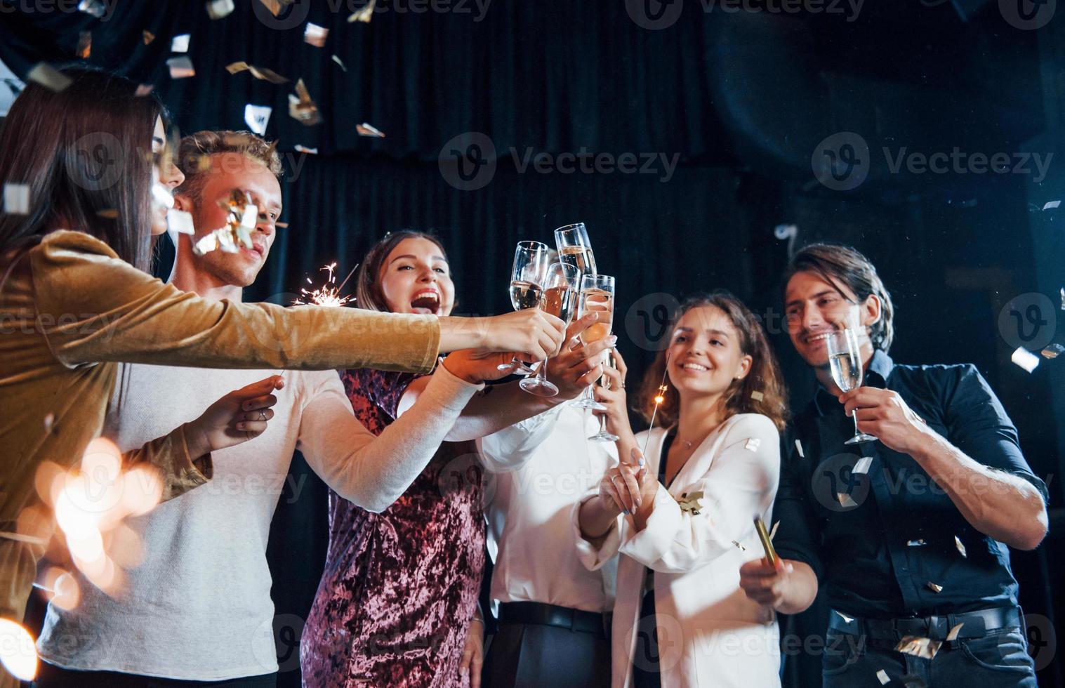 Knocking glasses. Group of cheerful friends celebrating new year indoors with drinks in hands photo