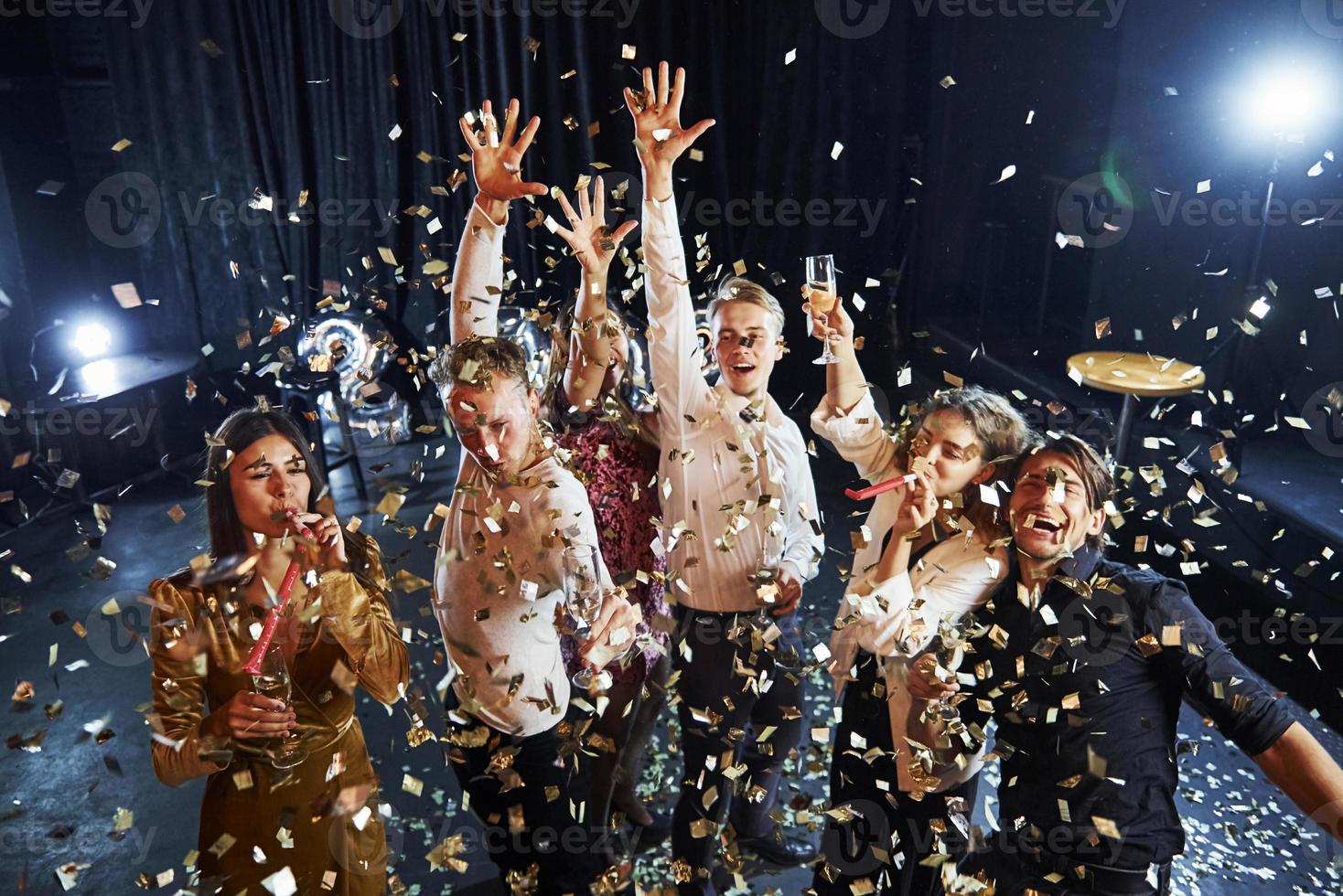 el confeti está en el aire. grupo de amigos alegres celebrando el año nuevo en el interior con bebidas en las manos foto