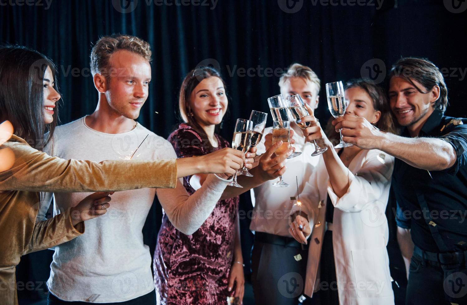 Knocking glasses. Group of cheerful friends celebrating new year indoors with drinks in hands photo