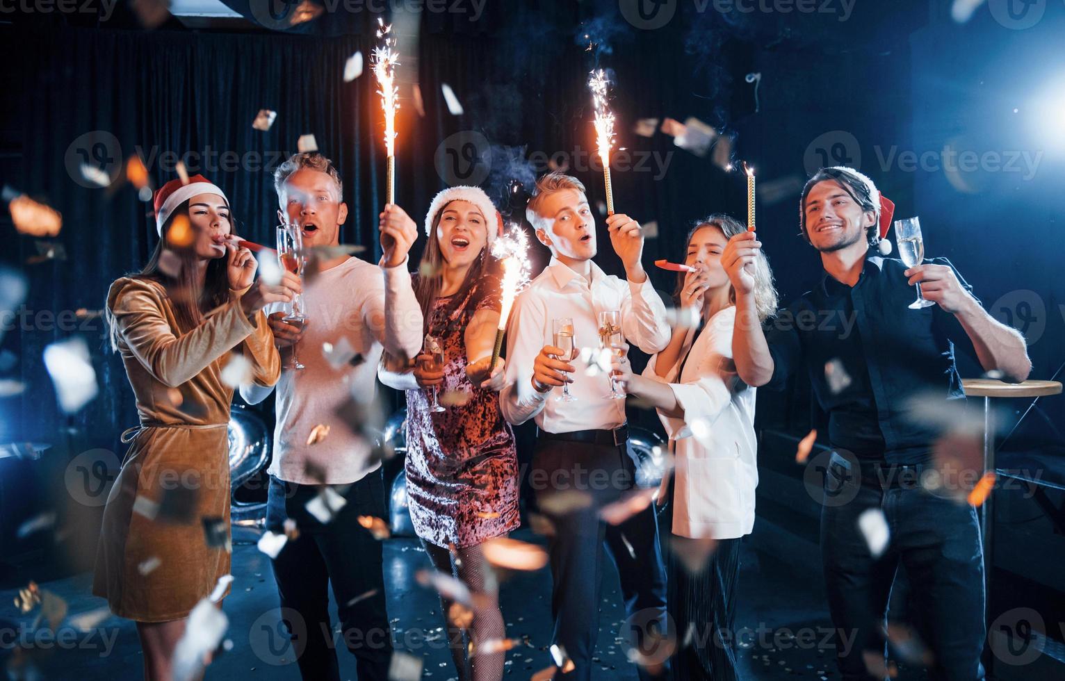 divirtiéndose con bengalas. grupo de amigos alegres celebrando el año nuevo en el interior con bebidas en las manos foto