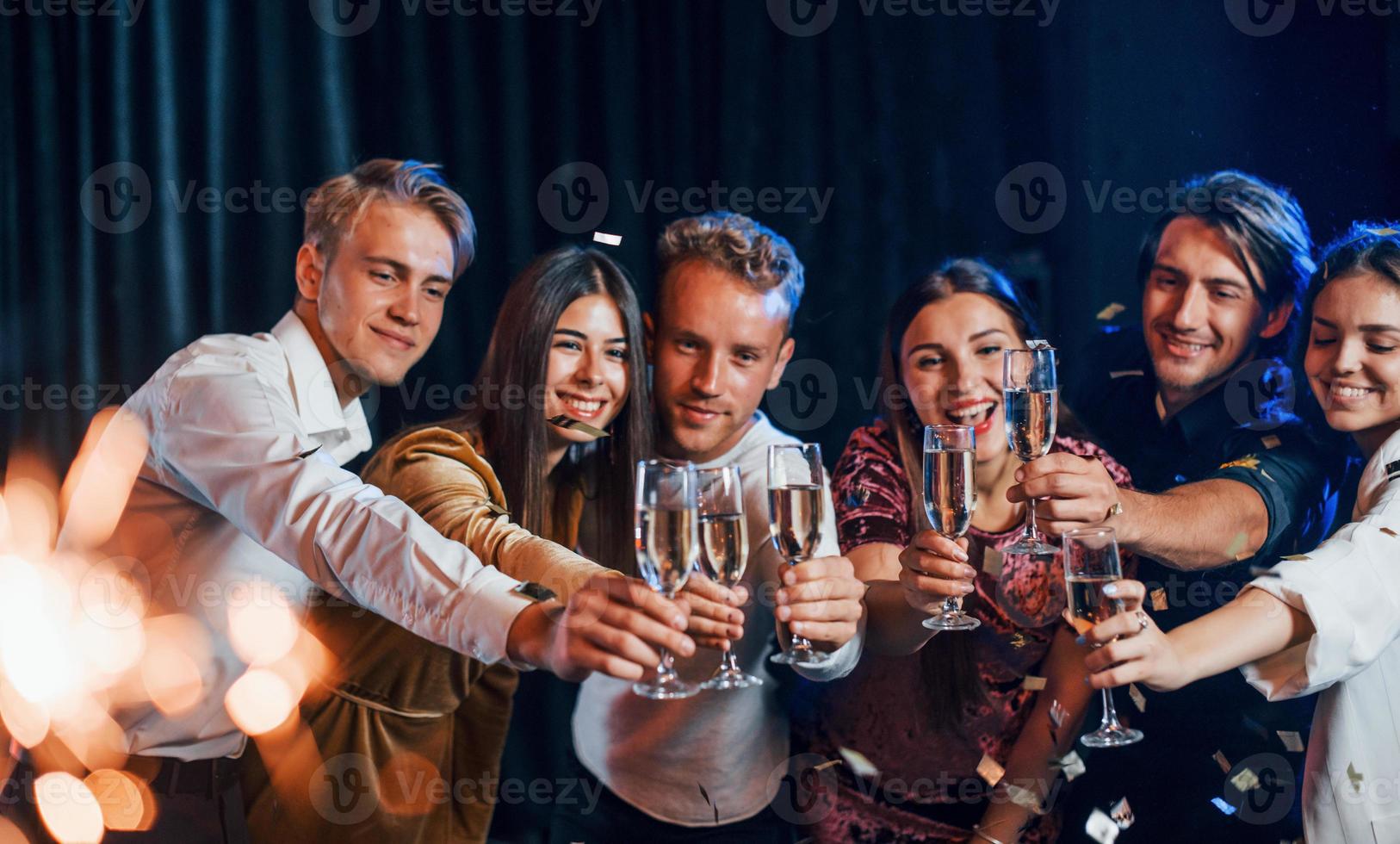Knocking glasses. Group of cheerful friends celebrating new year indoors with drinks in hands photo