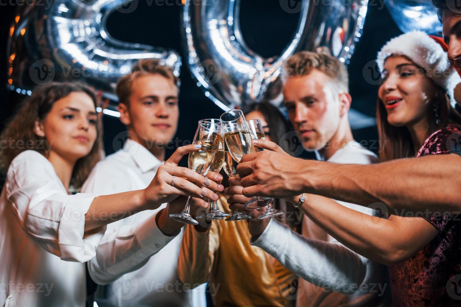 Knocking glasses. Group of cheerful friends celebrating new year indoors with drinks in hands photo