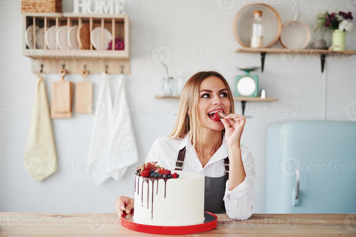 Positive blonde in indoors with her homemade pie holds fruit photo