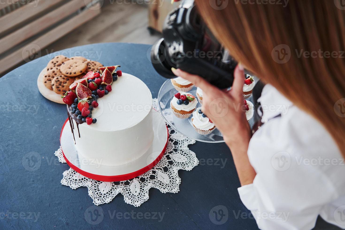 Woman stands in the kitchen and takes photo of her homemade cookies and pie by using camera