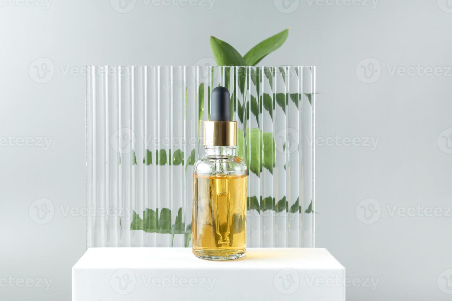 botella cosmética de vidrio con cuentagotas sobre un fondo de plexiglás con hojas de ruscus. aceite esencial natural y productos para el cuidado de la piel foto