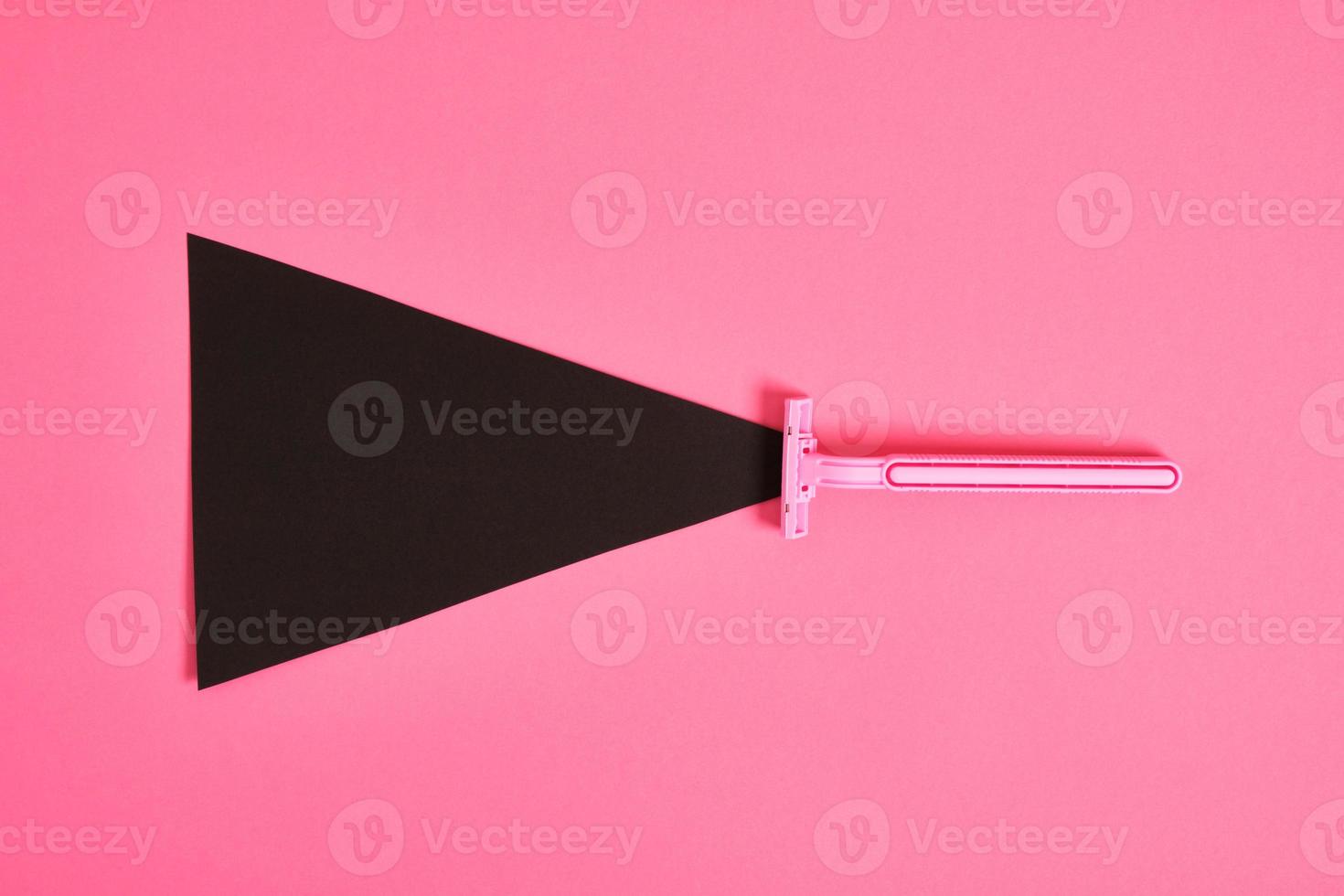 pink plastic disposable razor and black paper triangle on pink background photo