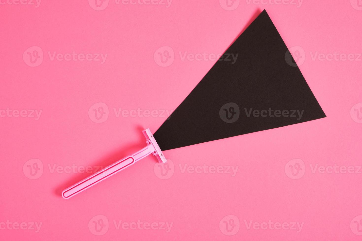 pink plastic disposable razor and black paper triangle on pink background photo