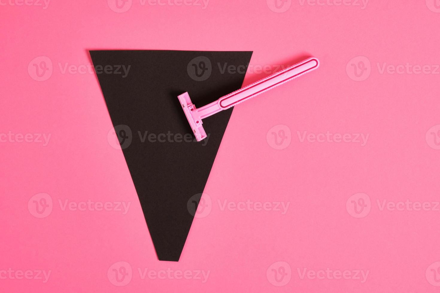 pink plastic disposable razor and black paper triangle on pink background photo