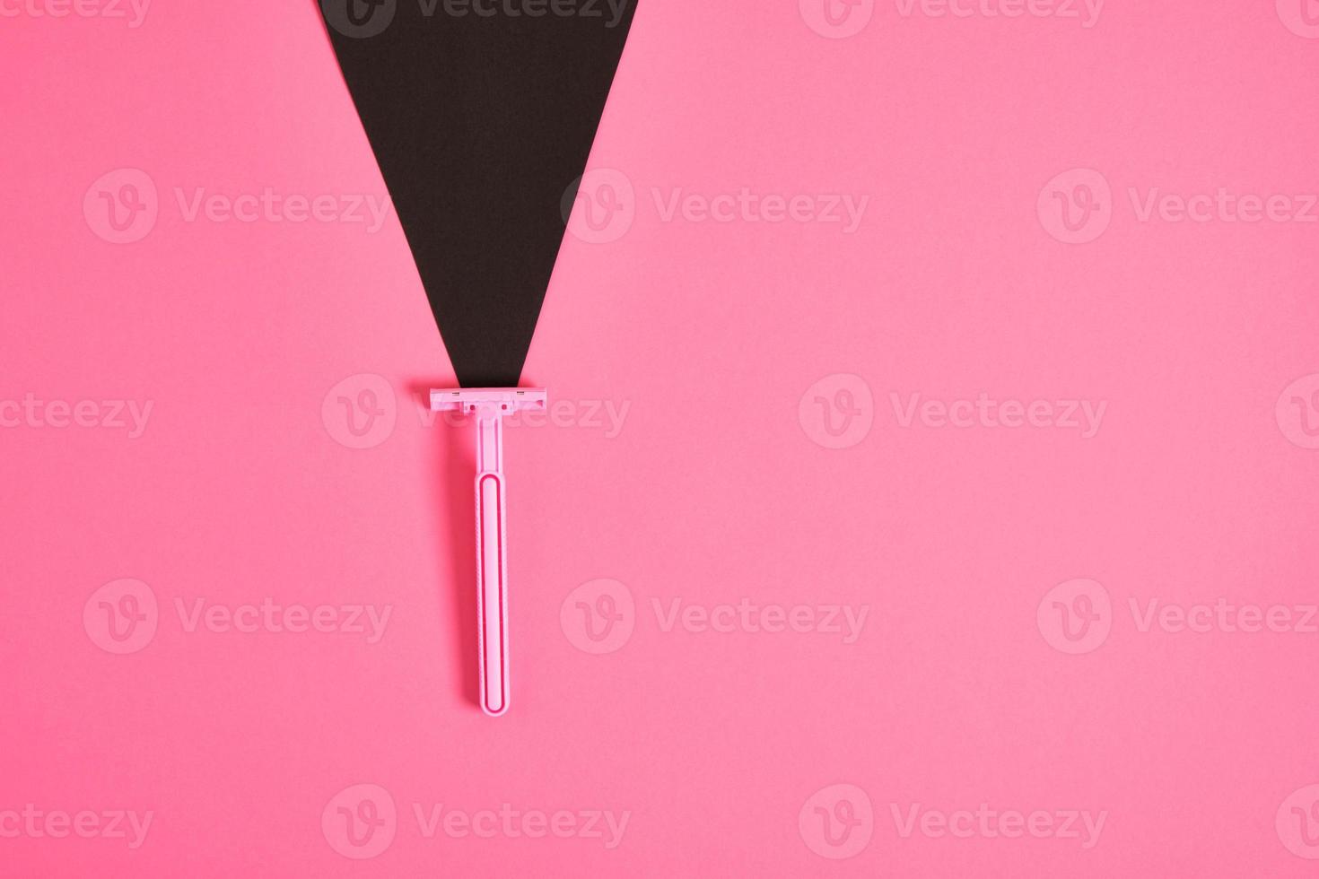 pink plastic disposable razor and black paper triangle on pink background photo