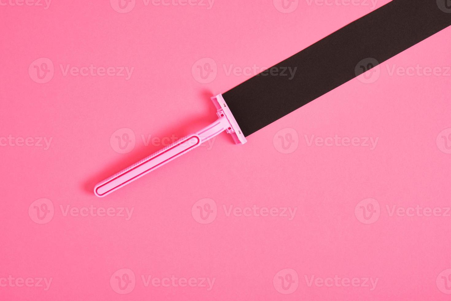 pink plastic disposable razor and black paper triangle on pink background photo