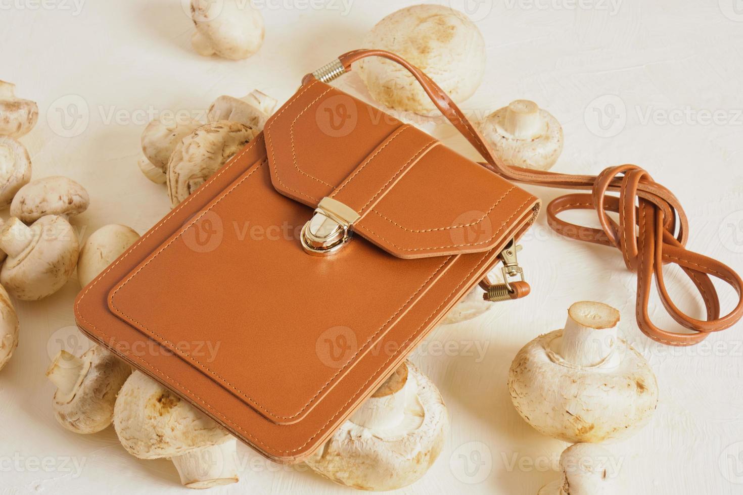 pequeña bolsa marrón para smartphone y tarjetas de crédito y champiñones sobre un fondo beige, concepto de cuero vegano foto