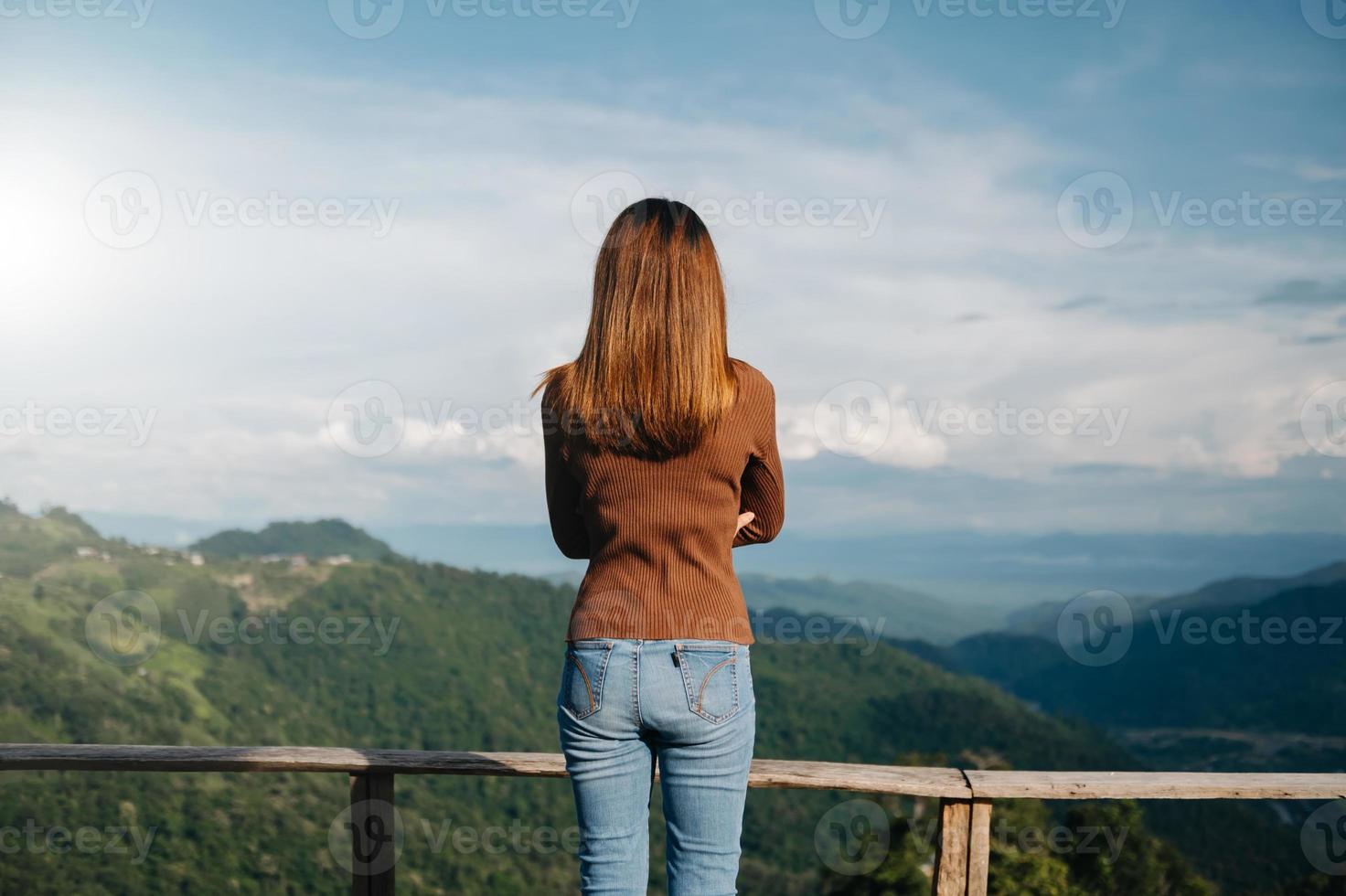 Rear view image of a woman traveler sitting and looking at a beautiful mountain,flower field and nature view photo