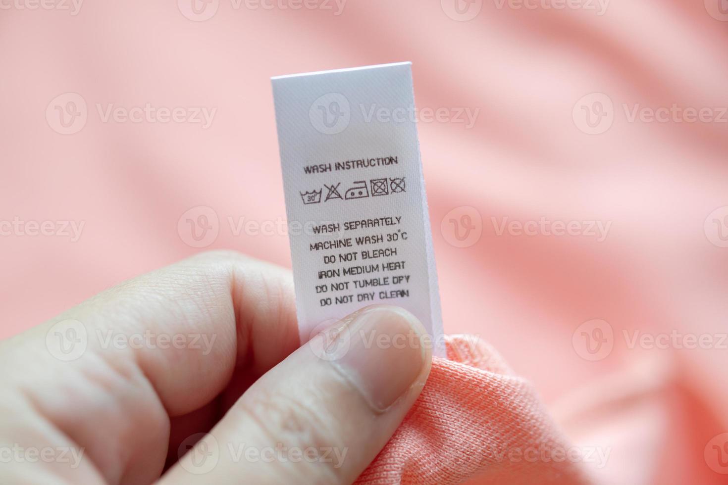 Hand hold and reading at white laundry care washing instructions clothes label on pink shirt photo