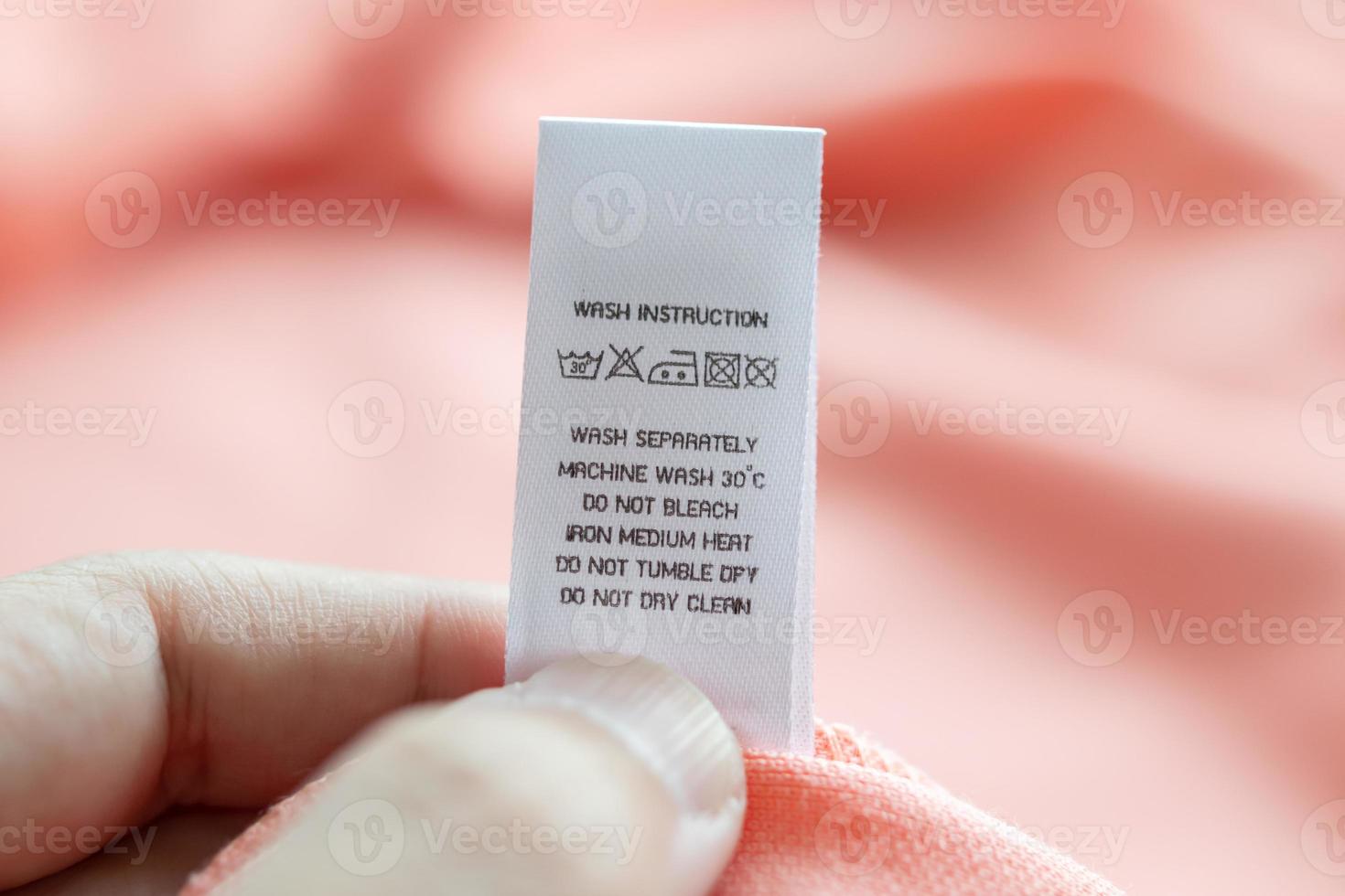 Hand hold and reading at white laundry care washing instructions clothes label on pink shirt photo