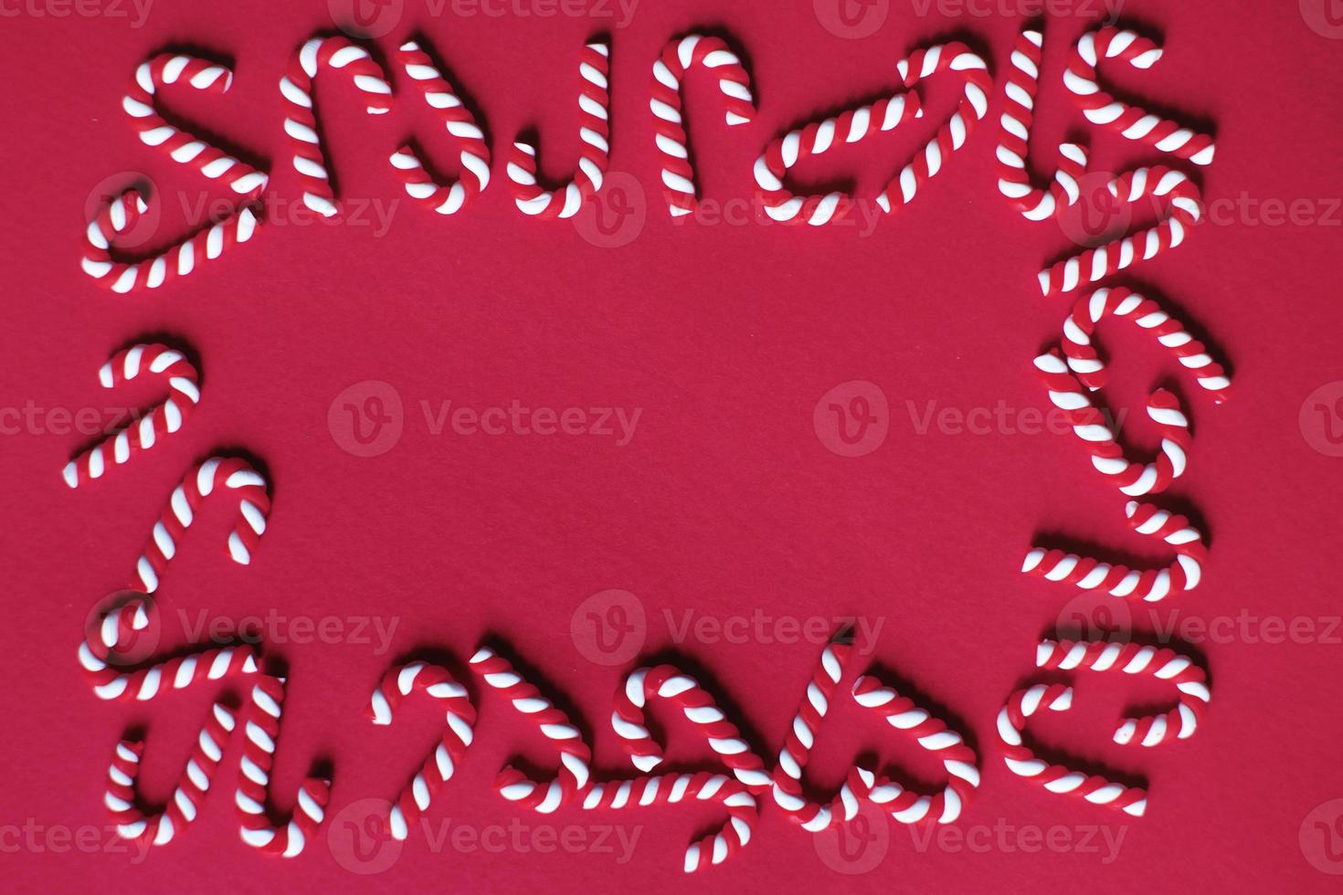 Flat lay Christmas composition with frame of candy canes on a red background. Copy space for text photo