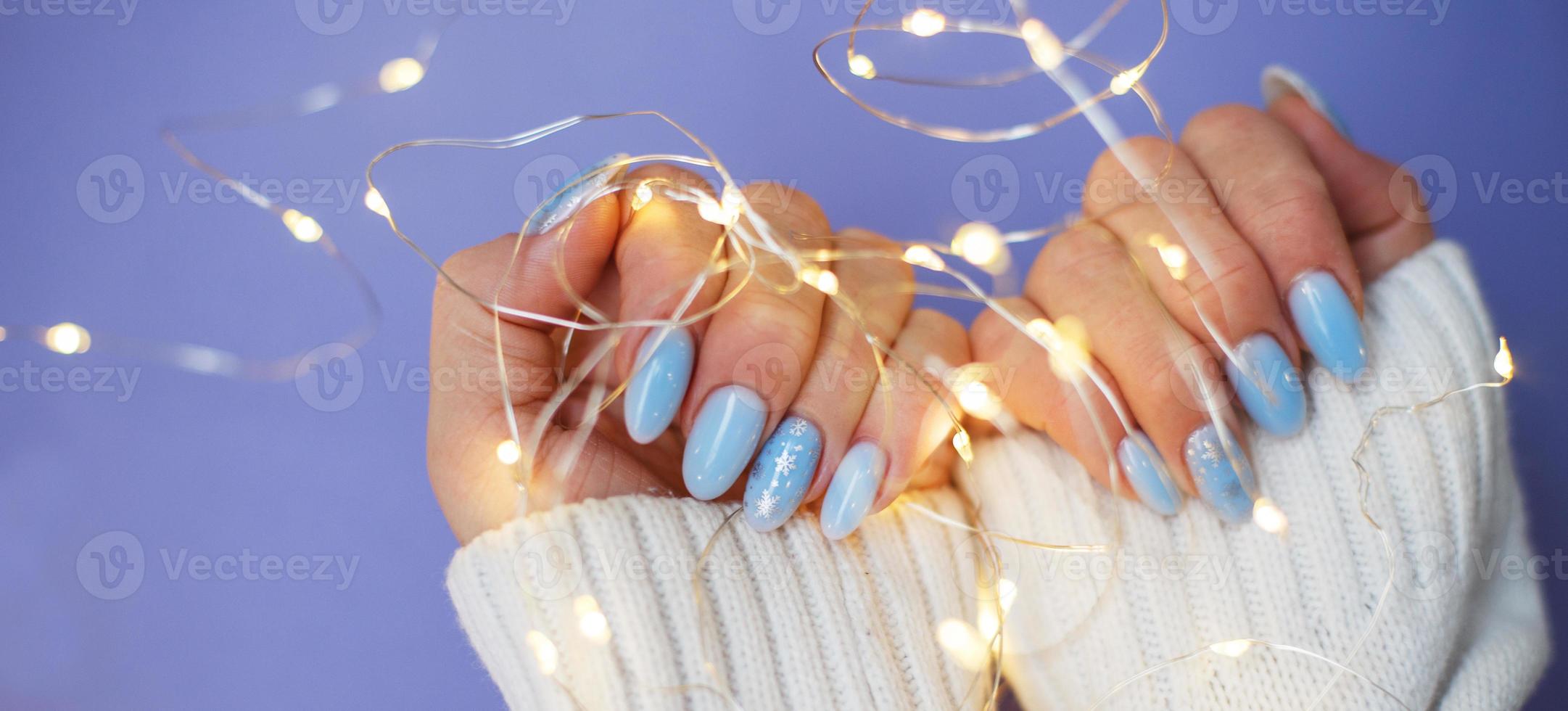 uñas acogedoras con manicura de invierno con copos de nieve y luces sobre fondo morado foto