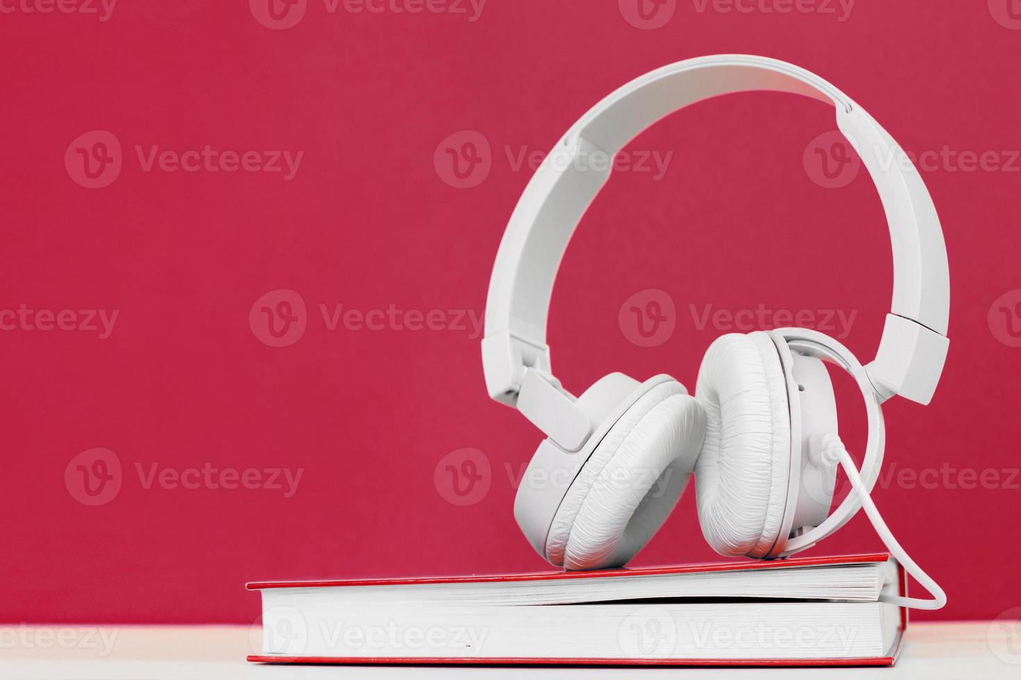 Audio book concept with headphones and a book on a viva magenta background. Listening to a book. photo