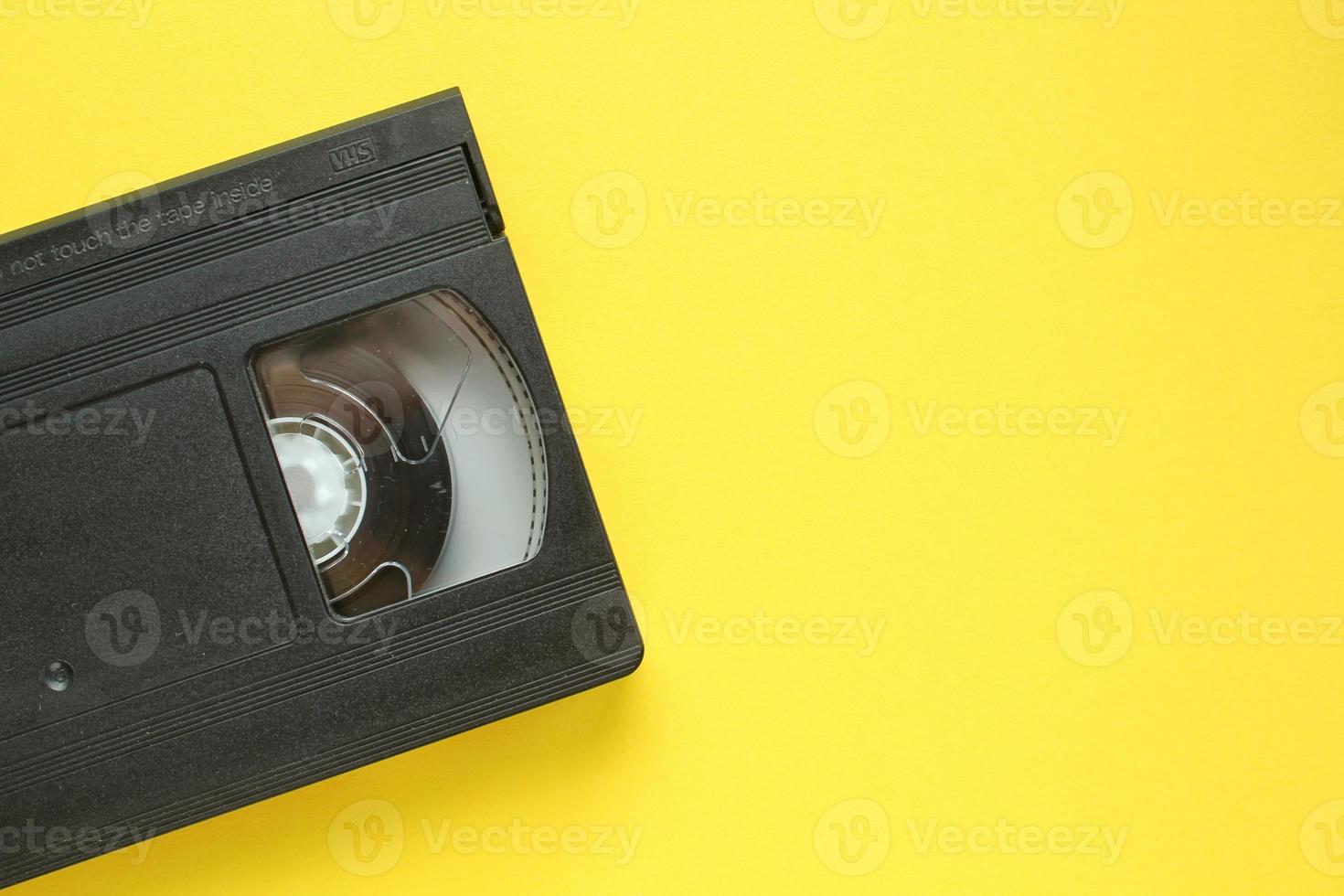 Black VHS videotape recorder cassette on yellow background. Old obsolete technology for tape recording and watching media movies. Retro, vintage, history, nostalgia concept. Top view, flat lay photo