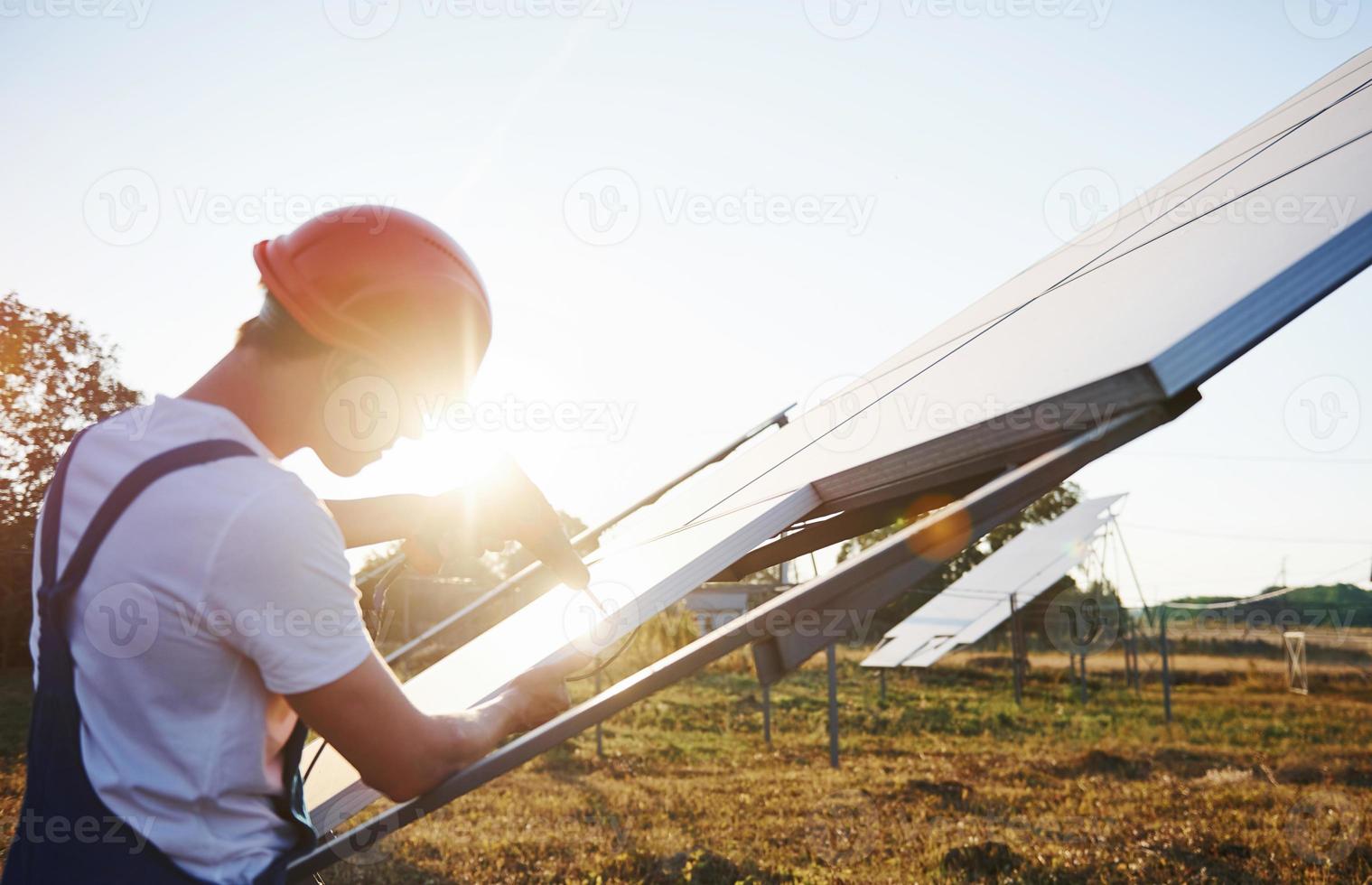 utilizando un destornillador inalámbrico. trabajador masculino en uniforme azul al aire libre con baterías solares en un día soleado foto