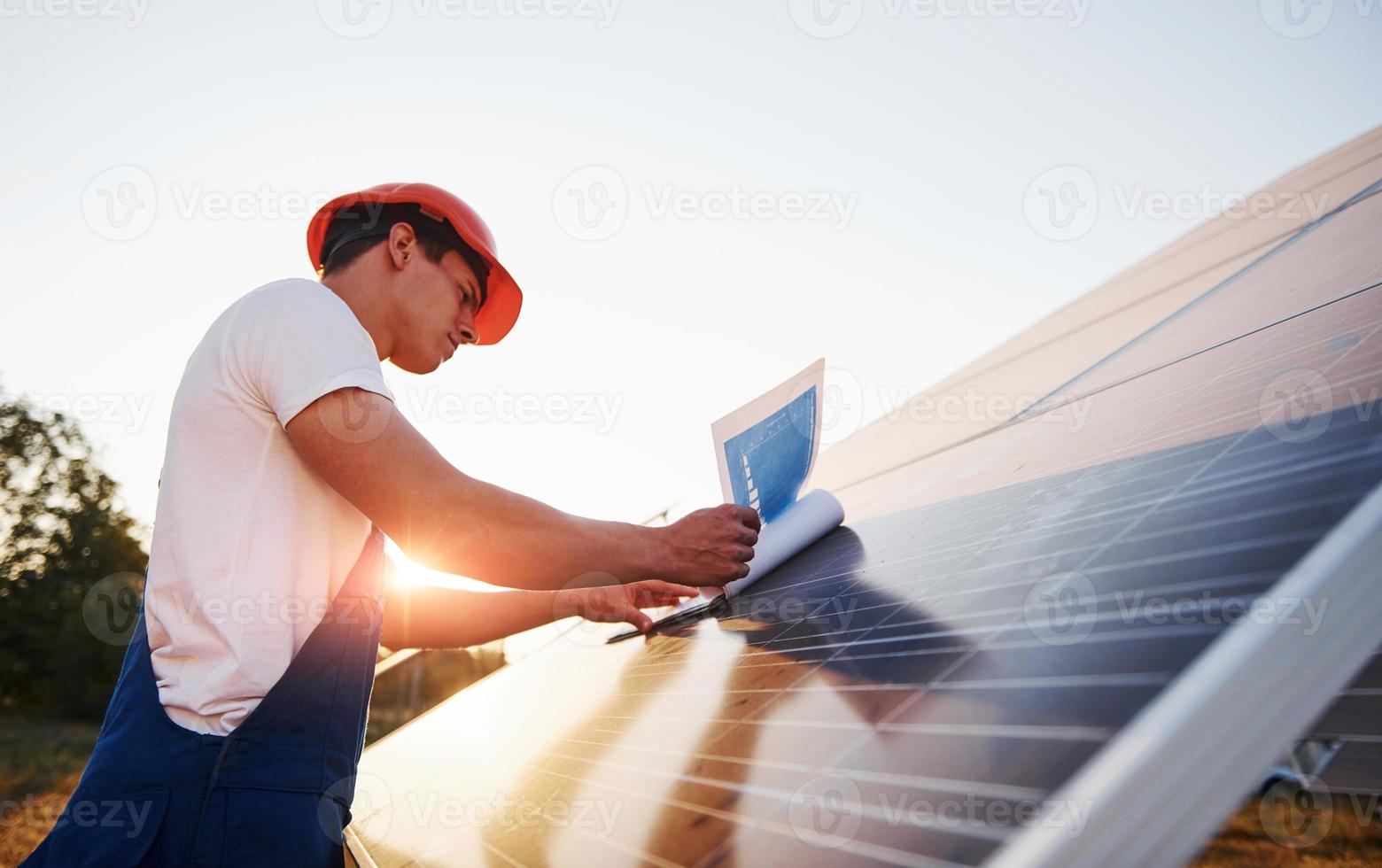 hermosa luz del sol. trabajador masculino en uniforme azul al aire libre con baterías solares foto