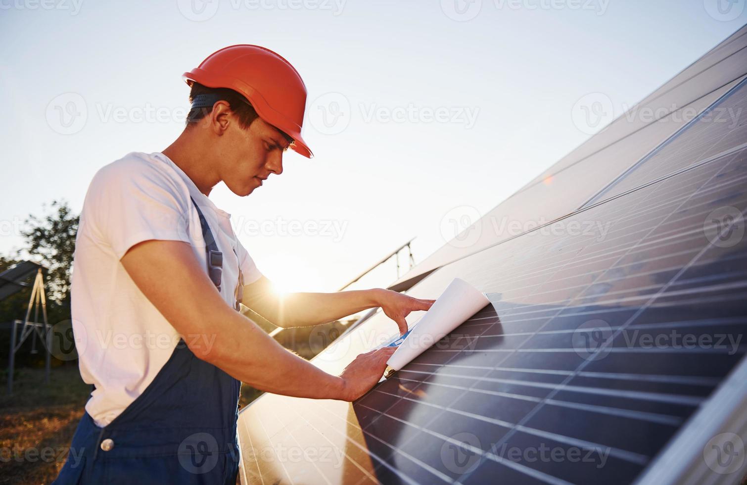 hermosa luz del sol. trabajador masculino en uniforme azul al aire libre con baterías solares foto