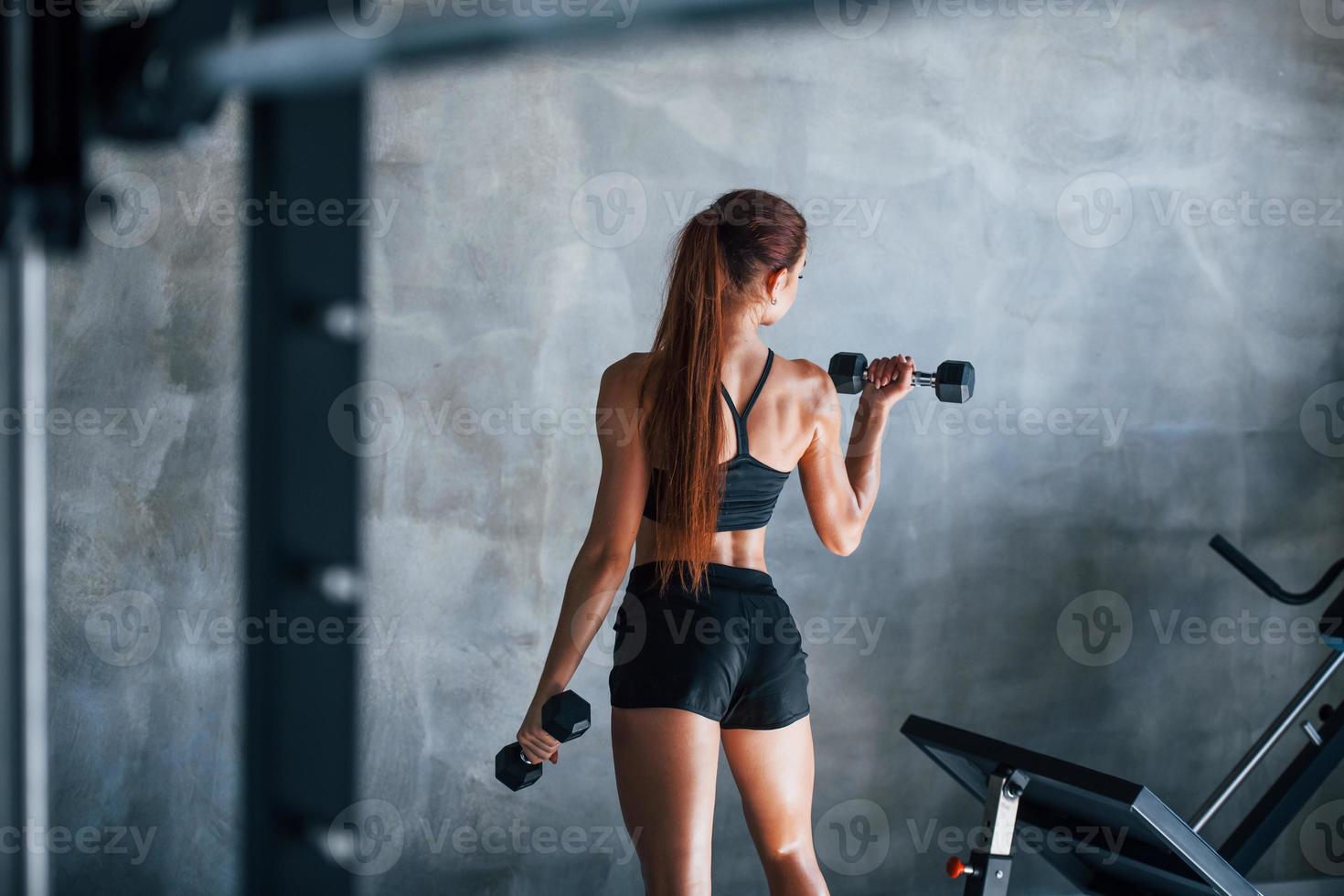 Young fitness woman with slim type of body and in black sportive clothes is in the gym photo