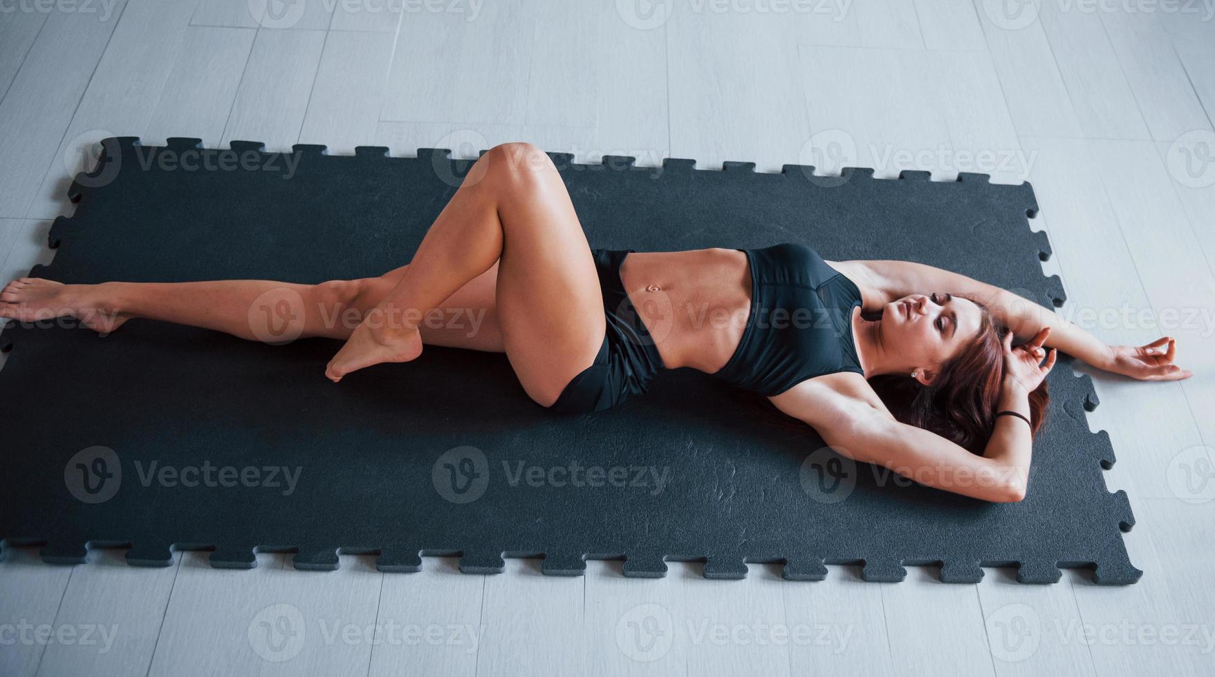 Young woman with slim type of body and in black sportive clothes lying down on the fitness mat photo