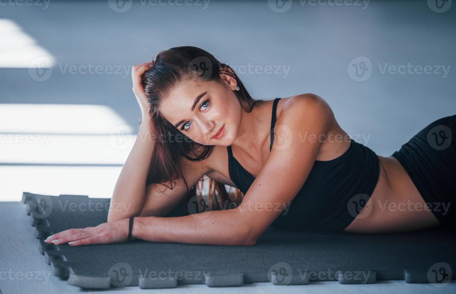 Young woman with slim type of body and in black sportive clothes lying down on the fitness mat photo