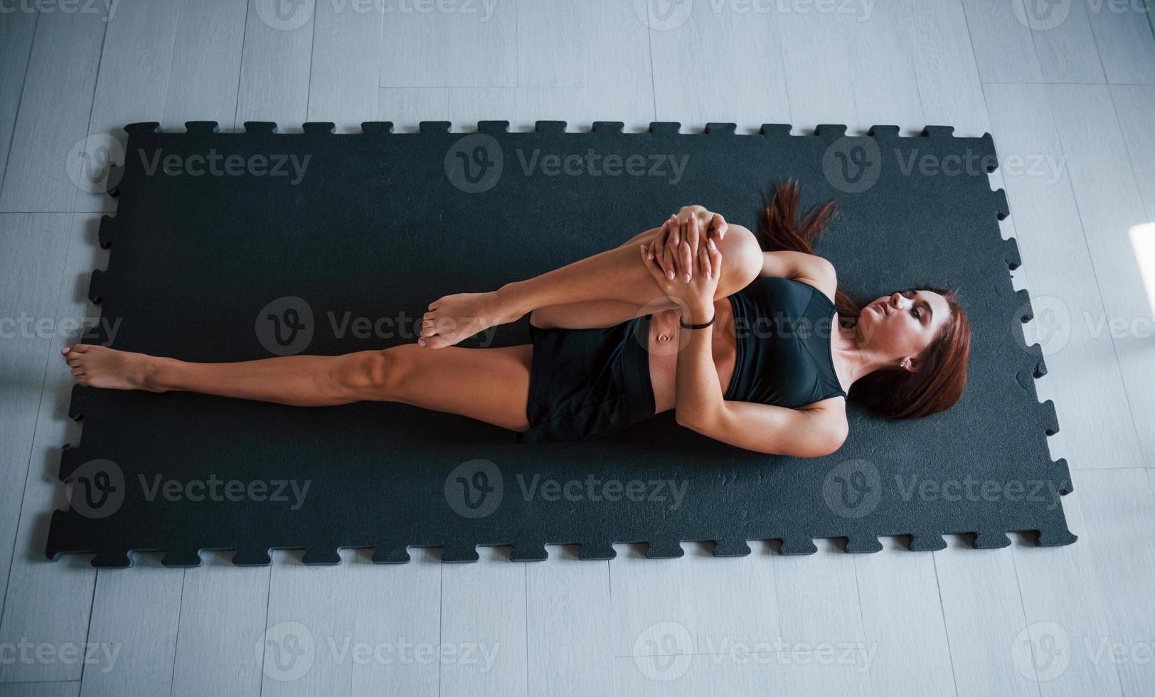 Young woman with slim type of body and in black sportive clothes doing yoga on the fitness mat photo