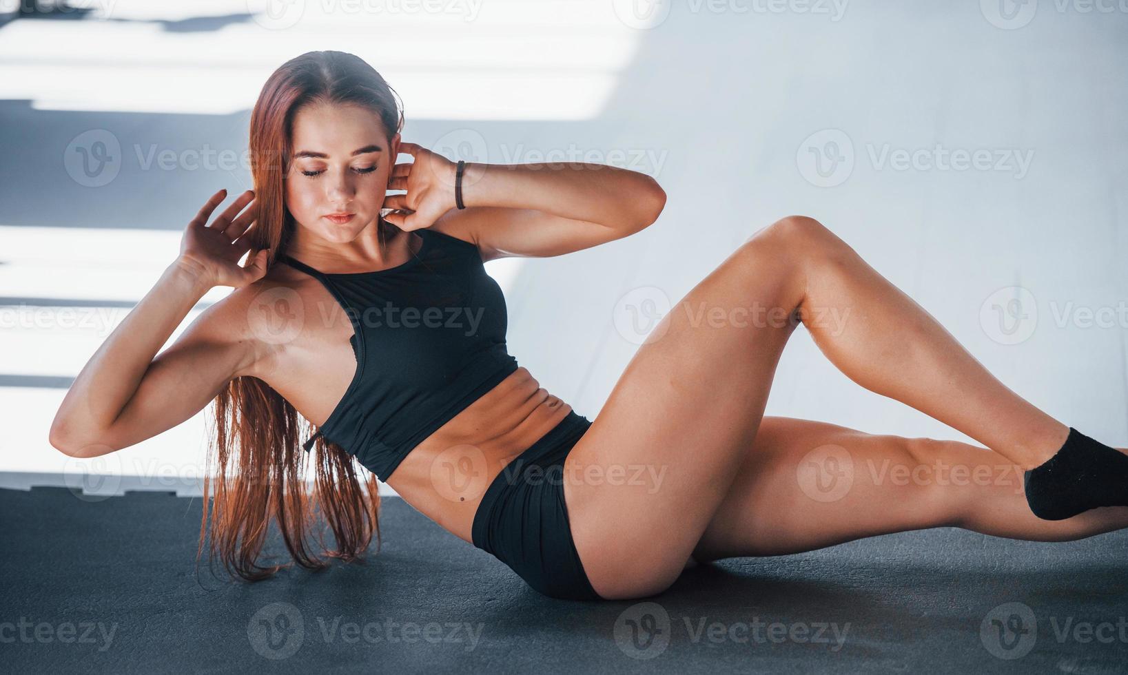 Doing abs. Young fitness woman with slim type of body and in black sportive clothes is in the gym photo