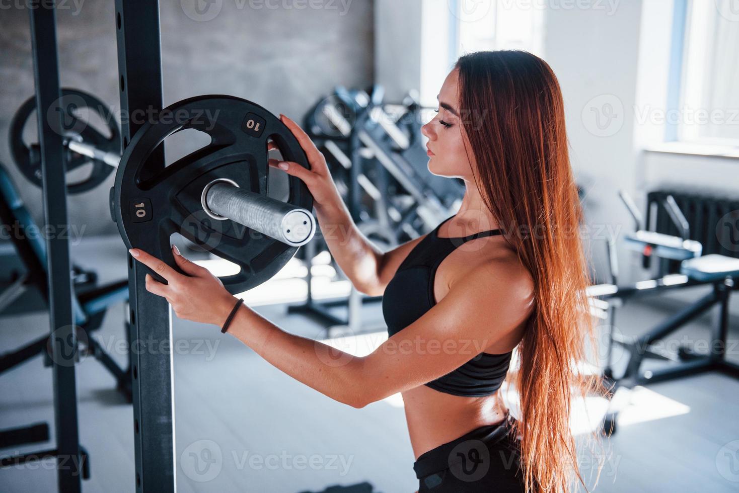 Young fitness woman with slim type of body and in black sportive clothes is in the gym photo