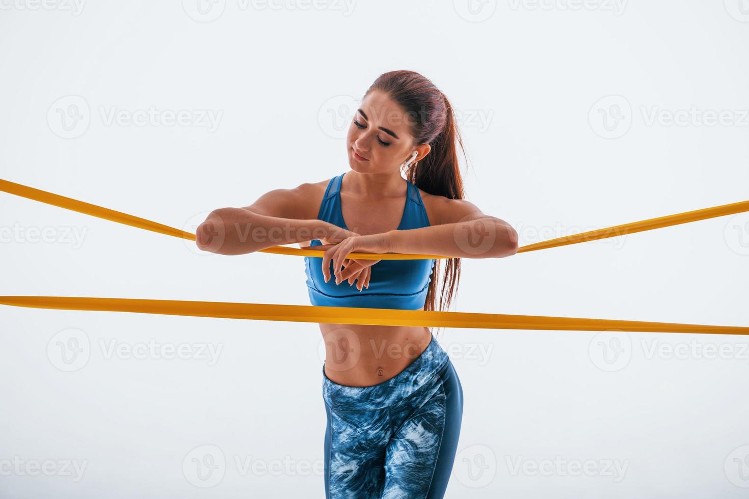 Leaning on yellow resistance band. Young woman with slim body type isolated against white background photo