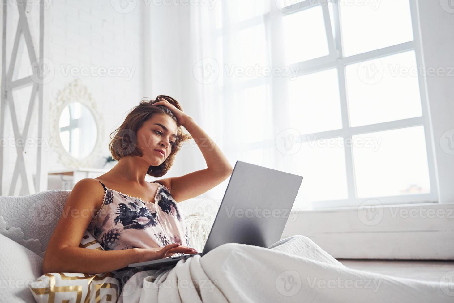 Cute girl lying on the bed with laptop in the bedroom at her weekend time photo