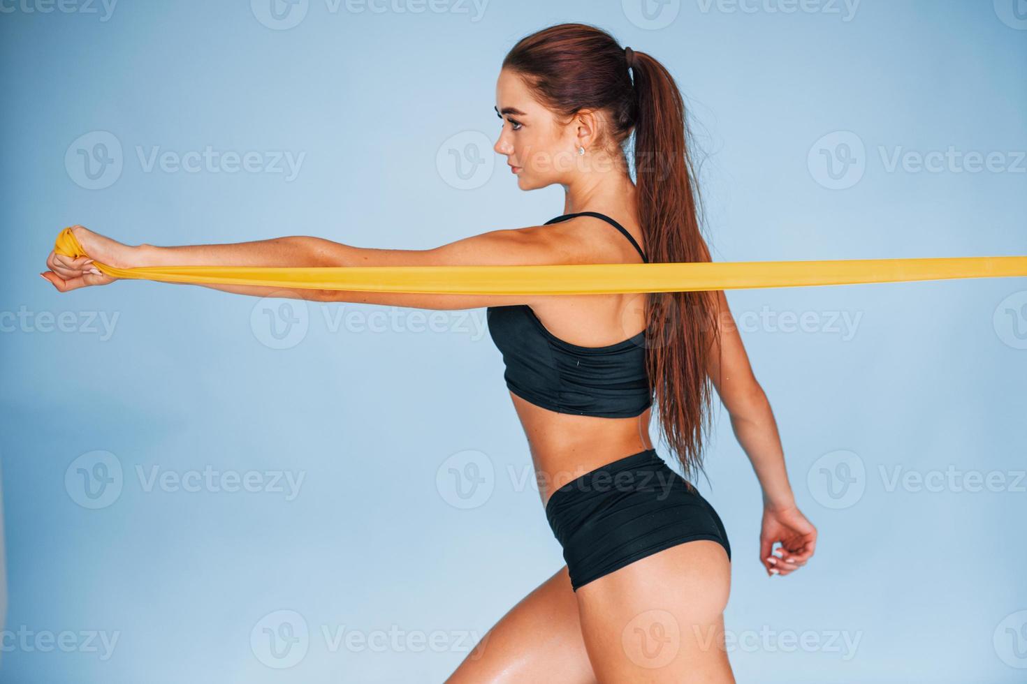 Hands exercise by using resistance band. Young woman with slim body type isolated against blue background photo