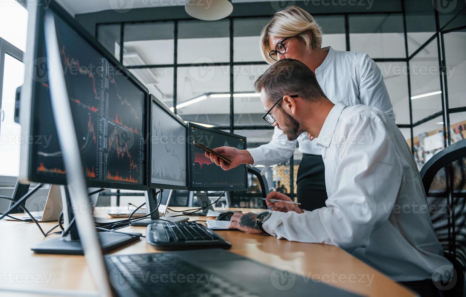 Analyzing information together. Two stockbrokers in formal clothes works in the office with financial market photo