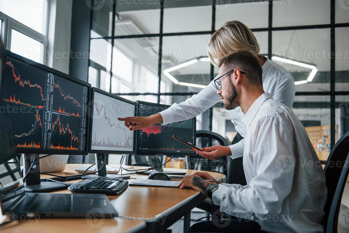 Analyzing information together. Two stockbrokers in formal clothes works in the office with financial market photo