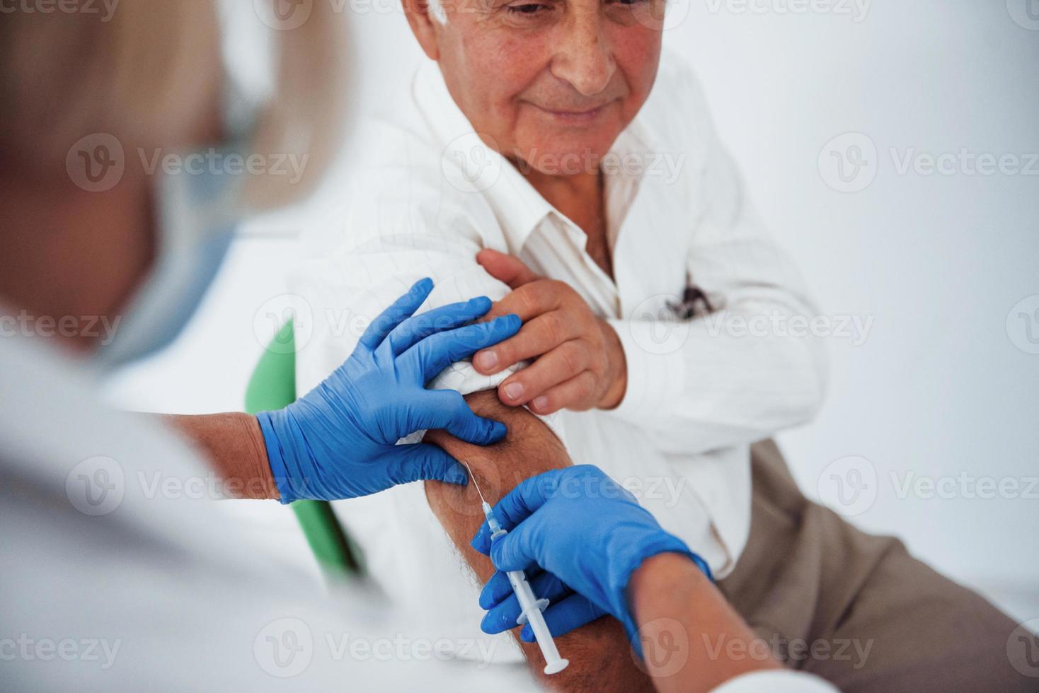Female doctor injecting senior male patient with syringe in the clinic photo